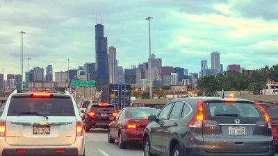 View from freeway traffic with many cars and brake lights heading into downtown Chicago with Sears Tower visible in skyline.