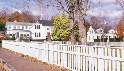 White picket fence along street with white two-story houses in the background in Wicasset, Maine.