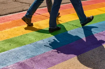 Close-up on legs of two people walking on rainbow-painted crosswalk.