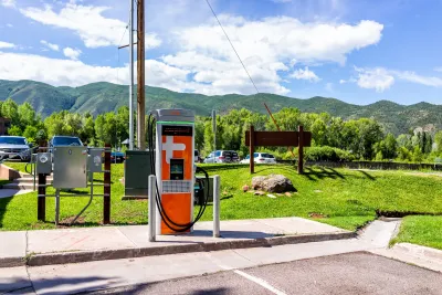 Orange EV charger in outdoor parking lot with Colorado mountains in background on sunny day.