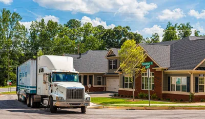 Large white moving truck pulling away from brick suburban single-family homes in Atlanta, Georgia.