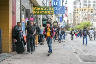 Austin's Sixth Street full of pedestrians during SXSW festival with yellow sign for Chuggin Monkey bar in foreground