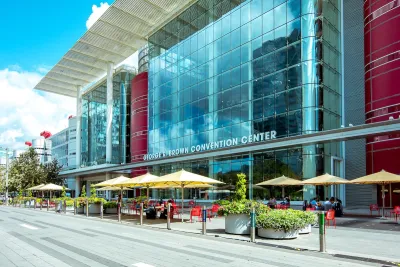 Front of George R. Brown convention center in Houston, Texas with yellow umbrellas over red tables in front.