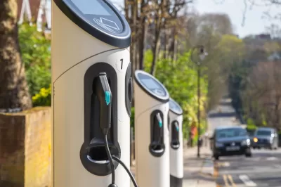 Row of curbside electric vehicle chargers with black car approaching in background