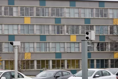 Two white traffic enforcement cameras above a road in Ottawa, Canada with a colorful multistory building in background