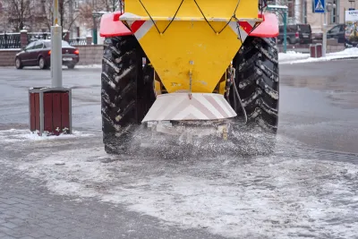 Yellow truck dropping salt onto a snowy road.
