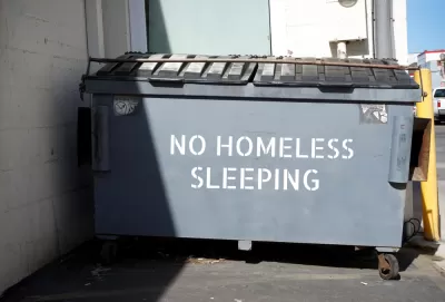 "No homeless sleeping" stenciled on grey dumpster in urban alley