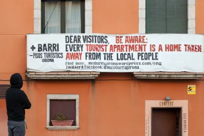 Sign saying “Dear visitors, be aware: every tourist apartment is a home taken away from the local people” hung on orange building in Girona, Spain.
