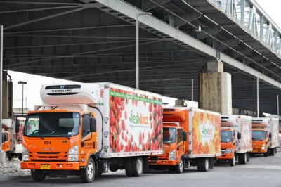 Row of refrigerated trucks with food delivery company logos under freeway overpass in the Bronx, NYC.