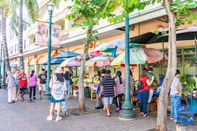 People walk down street with colorful umbrellas in front of ground floor retail in Honolulu, Hawaii.