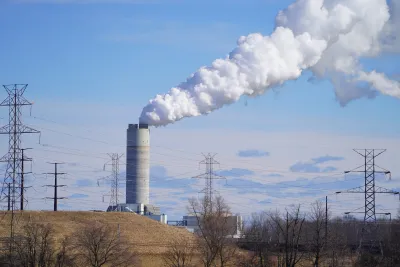 A tall, gray power plant billows smoke into a blue sky.