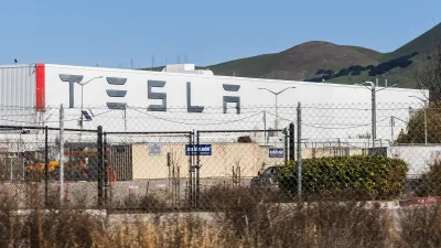 Tesla factory building in Fremont, California visible behind chain link fence.
