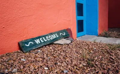 Green "welcome" sign leaning on wall of orange home with gravel ground in US Southwest.