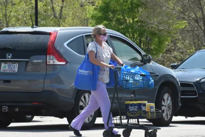 Woman pushing blue shopping cart in parking lot next to grey Honda SUV.