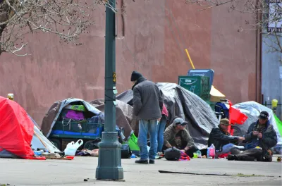 Unhoused people and tents surrounded by everyday items on sidewalk in Denver, Colorado.