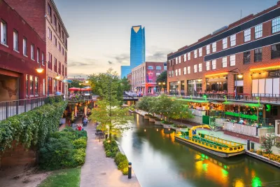 Canal in downtown Oklahoma city with outdoor dining patios on either side and tall modern skyscraper in background.
