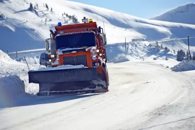 Orange snowplow clearing snow on Colorado road