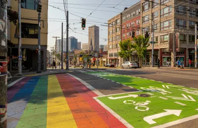 Crosswalk in Seattle, Washington with green painted bike lane and rainbow-painted crosswalk and electric cables for transit cars above.