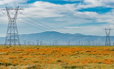 Power transmission lines surrounded by orange California poppies and silhouette of mountains in background