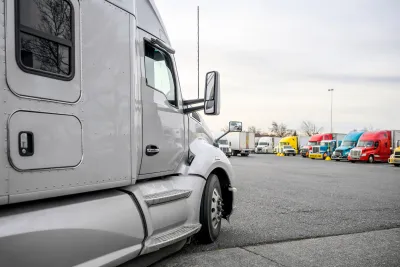 White big rig truck parked in lot with other colorful trucks visible in background.