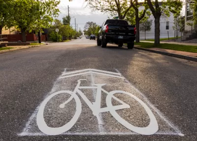 Street-level view of sharrow symbol on asphalt with parked car in background