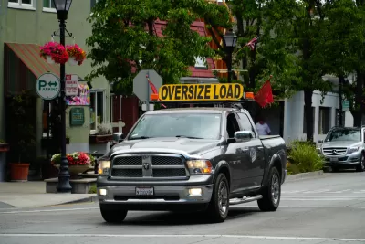 Pick-up truck on small town street with yellow "Oversize Load" sign 