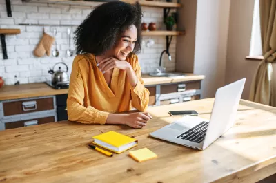 Woman in yellow top sitting at wood kitchen island looking at laptop