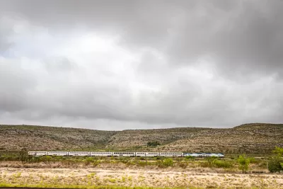 Amtrak Sunset Limited train viewed from the side passing low desert hills in West Texas