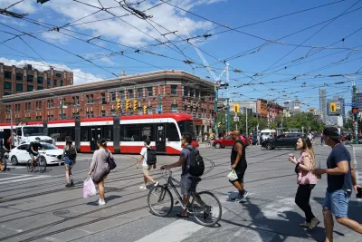 Red streetcar on busy street intersection with public transit wires overhead in Toronto, Canada.