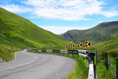 Asphalt road with yellow and black turn warning signs winding through green Welsh mountain landscape