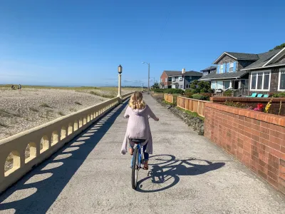 Woman in pink sweater rides a beach cruiser bicycle on a paved trail next to the beach in Seaside, Oregon.
