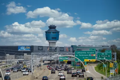 Freeway with traffic leading to LaGuardia Airport with air control tower in the background against white fluffy clouds on bue sky