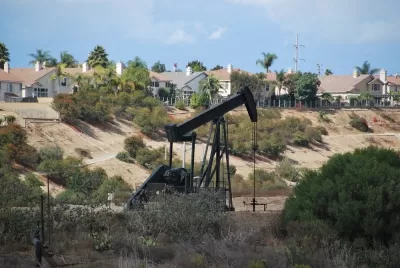 Black pumpjack oil derrick with houses in background