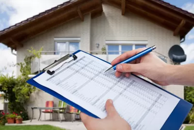 Person holding clipboard with checklist and pen with blurred house in the background