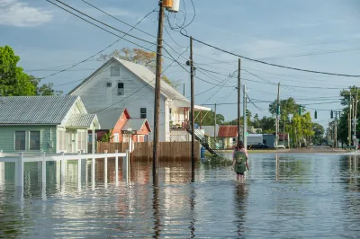 Two people walk through flooded street with wood homes in Louisiana.