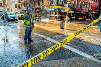 Utility worker stands in flooded New York City intersection roped off with yellow caution tape speaking on walkie talkie.