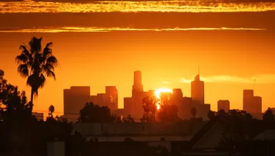 View of Los Angeles skyline against a bright orange sky with a palm tree at left
