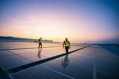 Solar panels on a rooftop with two workers in hard hats and safety vests walking between panels