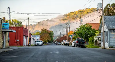 Colorful wood buildings line wide asphalt street in West Virginia small town with misty hills in background.