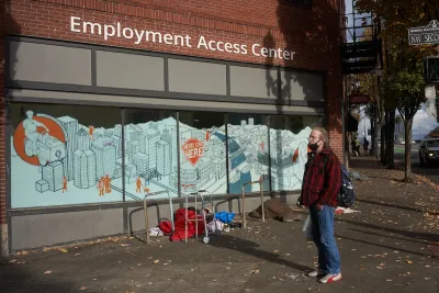 Man wearing red and black plaid shirt stands in front of employment center office in the ground floor of urban office building.