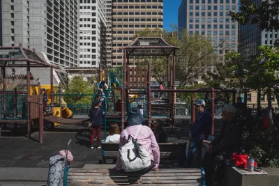 Adults watching over children playing on urban playground in Chinatown, San Francisco with high-rises in background.