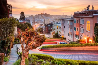 View of downtown San Francisco from top of windy street at sunset with Coit Tower in distance