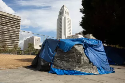 A tent covered in blue and black tarps sits on a downtown Los Angeles sidewalk with the white ziggurat-topped L.A. City Hall looming in the background