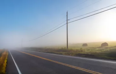 Foggy rural road with power lines and haystacks along the side