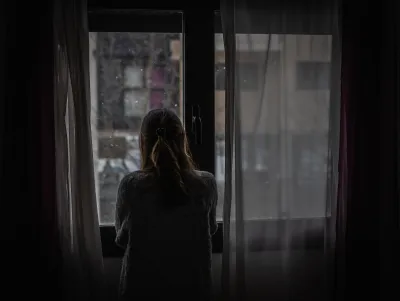 Woman stands in front of window looking out at rain in a dark room.