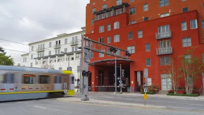 Silver and yellow Los Angeles Metro train going into bottom floor of red building with apartments in top floors.