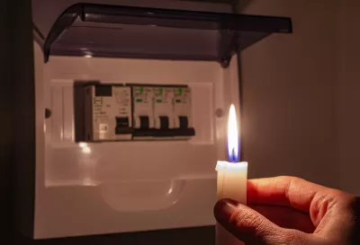 Hand holding candle toward small electrical fuse box in the dark