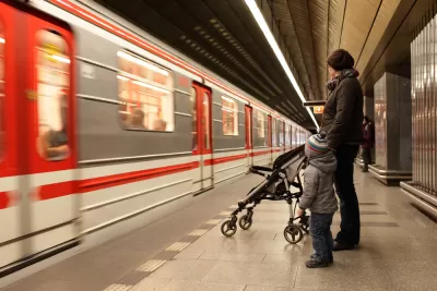 Woman with child and stroller waiting on Prague subway platform with blurred train passing by.