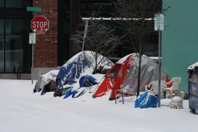 Tents set up by unhoused people surrounded by assorted everyday items on snowy Portland sidewalk.