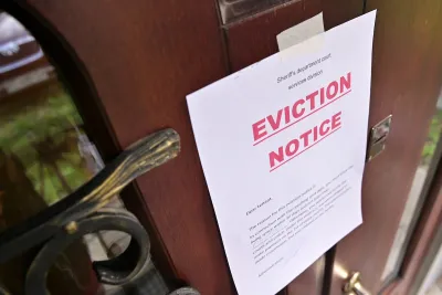 Eviction notice with bold red "Eviction Notice" text taped to brown wooden door.